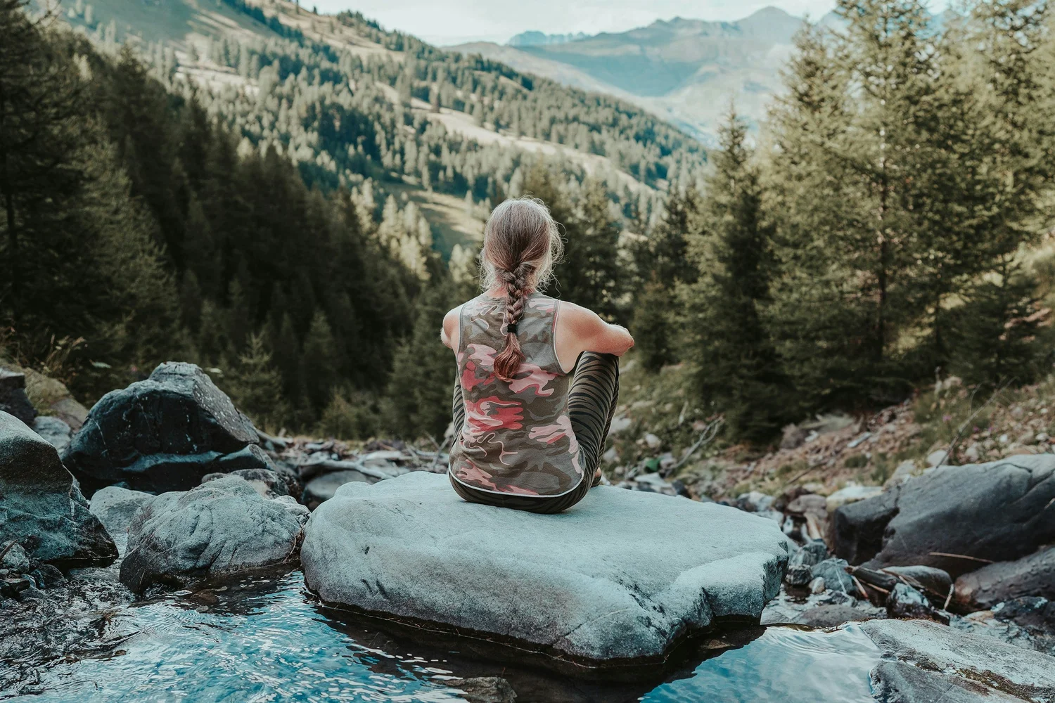 A woman who healed the trauma that was troubling her sits on a rock overlooking a valley, feeling free and happy